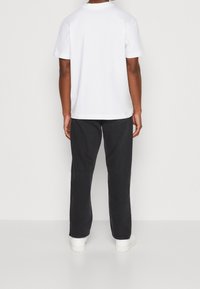 Camiseta blanca de manga corta con escote redondo, combinada con pantalones rectos negros y zapatillas blancas, vista desde atrás.