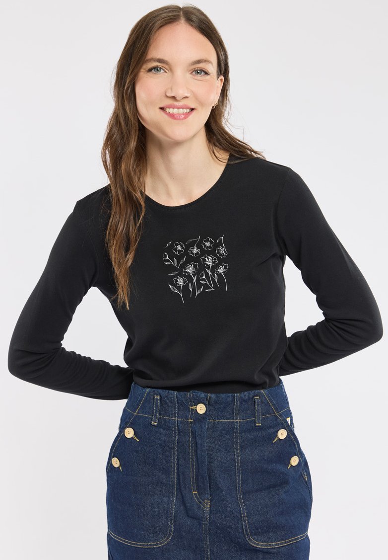 Chemise noire à manches longues avec un motif floral blanc sur la poitrine, associée à une jupe en denim taille haute avec des accents de boutons.