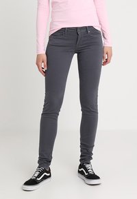 Szare bawełniane legginsy skinny z pięcioma kieszeniami i zapięciem na guzik, zestawione z czarnymi trampkami i różową bluzką z długim rękawem.