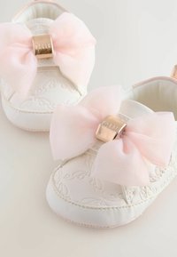 Scarpe bianche in pelle con un design floreale embossato, caratterizzate da ampi fiocchi rosa chiaro e dettagli in hardware dorato sulla parte anteriore.