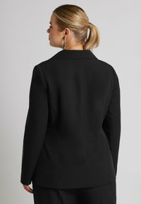 Svart skräddarsydd kavaj med en strukturerad passform, med skarpa slag, långa ärmar och en slät tygtextur. Bakvy visas.