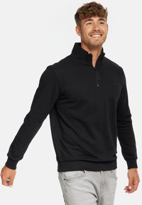 Sweatshirt noir à col zippé demi, avec des poignets et un ourlet côtelés, fabriqué dans un tissu lisse. Détail minimal du logo sur la poitrine.