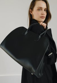 Schwarze Lederhandtasche mit glatter Textur, runder Form und zwei langen Griffen. Verfügt über ein einfaches Design ohne sichtbare Hardware oder Muster.