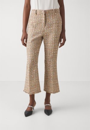 Vrouw in een verkorte, veelkleurige tweed broek met franjes aan de onderkant en zwarte puntige hakken met zilveren banden.
