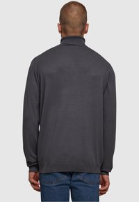 Grauer Rollkragenpullover aus glattem Strickstoff, mit langen Ärmeln und geripptem Kragen, kombiniert mit blauen Jeans.