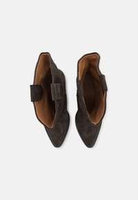 Bruna mockaskinnsankelstövlar med spetsiga tår, beige innersulor och korta, breda dragflikar på vardera sidan för enkel påtagning.