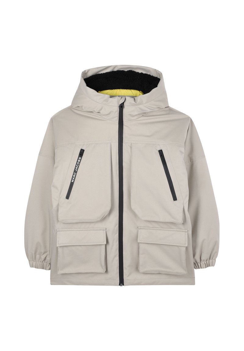 Veste imperméable beige avec capuche, dotée de deux grandes poches avant, de deux poches latérales zippées et d'une doublure contrastante noire et jaune.