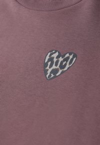 Tissu mauve avec un petit patch en forme de cœur présentant un motif léopard près de l'encolure.