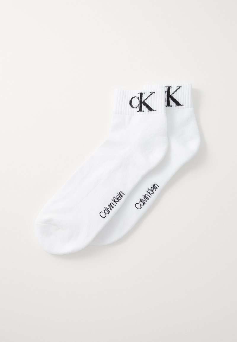 Biele bavlnené ponožky s rebrovanými manžetami, s čiernymi iniciálmi "ck" na prednej strane a s nápisom "Calvin Klein" na boku.