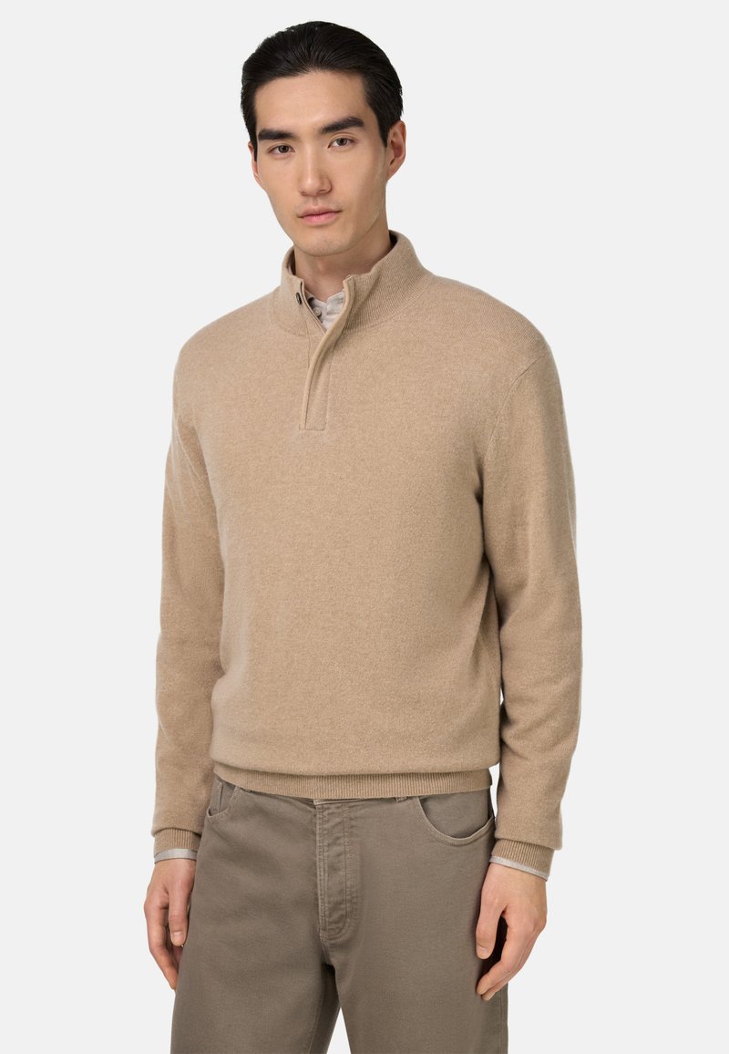 Beige pullover sweater with a quarter-zip collar, ribbed cuffs, and hem. Fabric appears soft with a subtle texture. Worn over a lighter shirt.