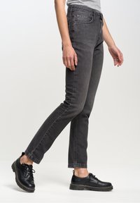 Jean noir au design droit classique, fabriqué en denim avec une texture lisse et des détails de couture subtils. Assorti avec des chaussures noires.