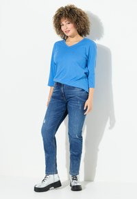 Top de manga larga azul en forma de V, combinado con jeans azules desgastados y botas de tobillo plateadas con suelas negras. Textura suave, corte relajado.