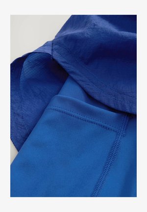 Sinine sportlik ülikond sileda tekstuuriga, millel on lõtv istuvus. Üle on kihtidega sobivad sinised kitsad retuusid, millel on veniv vöökoht.