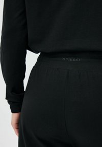 Czarne casualowe spodnie z elastycznym pasem z logo "DIVERSE". Miękka tekstura i dopasowany krój zwiększają komfort noszenia.