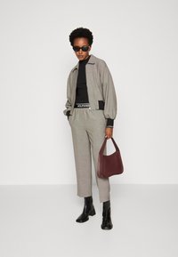 Grau karierter Bomberjacke, schwarzer Rollkragenpullover, taillierte Hose, schwarze Absatzstiefel und einer bordeauxfarbenen Handtasche. Einfaches Design mit ausgeprägten Texturen.