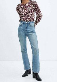 Blouse florale multicolore avec un col rond et un détail en forme de trou de serrure, associée à un jean taille haute bleu clair à jambes droites et des bottes à talons carrés noires.