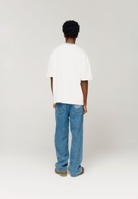 Hvit oversized T-skjorte med korte ermer, sammen med blå, løstsittende jeans. Jeansene har detaljer med stikking på baklommene.