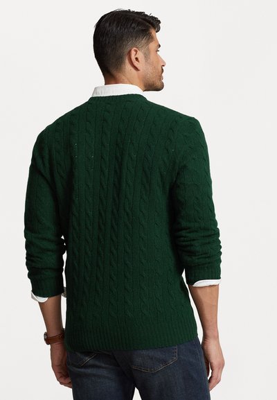 Suéter de punto trenzado verde oscuro con dobladillo de canalé, mangas largas y detalle de cuello blanco asomando por debajo. Tejido texturizado con un aspecto acogedor.