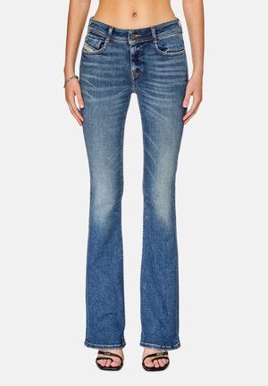 Vue de la taille vers le bas d'une personne portant un jean bootcut taille haute bleu et des sandales noires à bout ouvert avec une fine bride.