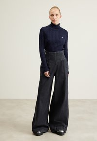 Maglione a collo alto a coste color navy abbinato a pantaloni in denim neri a gamba larga e alta vita. Scarpe nere chunky completano l'outfit.