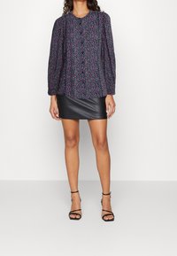 Blusa a fiori in tessuto scuro, con maniche lunghe e scollatura rotonda, abbinata a una mini gonna in pelle nera e tacchi con cinturini.