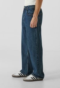Vide ben denim jeans i mørkeblå vask, med klassisk fem-lommers design, knappestenging og lett falming langs sømmene.