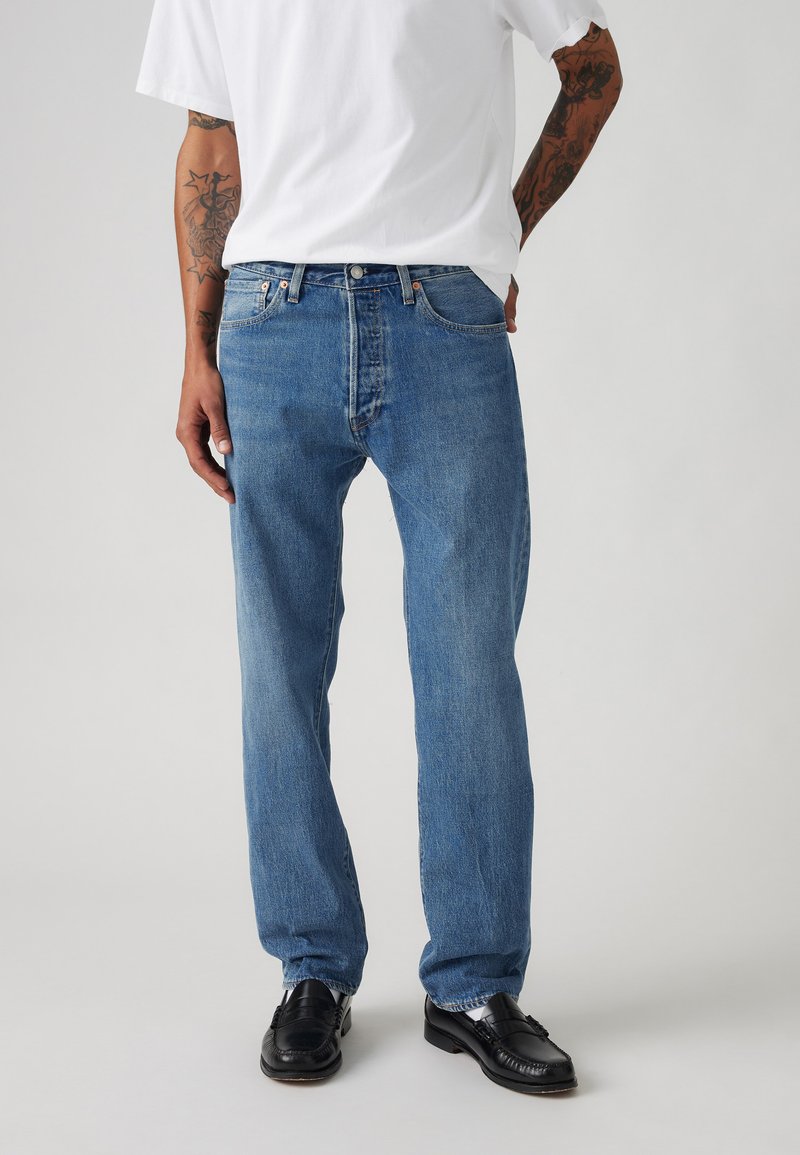 Light blue denim jeans with a straight leg design, five-pocket style, and a stitched waistband. Paired with black shoes and a white shirt.