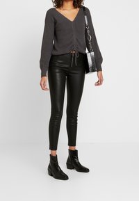 Kolgrå rämmad tröja med V-ringning och knytdetalj, i kombination med glänsande svarta faux läderleggings och svarta ankla stövlar.