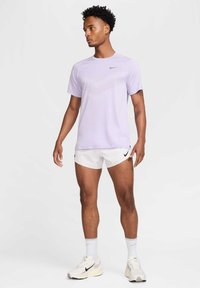 Light purple athletic t-shirt with short sleeves and a patterned texture. Paired with white shorts featuring a black logo. White sneakers.