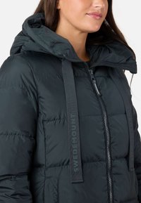 Sort pufferjakke med høj krave og hætte, med lynlås, sidelommer og mærkede grå stropper på forsiden.