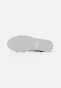 Suola di sneakers bianche con texture incisa e branding sottile. Punta arrotondata, bordi lisci e design piatto e flessibile per il comfort.