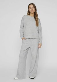 Pilkos spalvos džemperis ir plačių kelnių komplektas, pagamintas iš minkštos medvilnės mišinio. Viršus turi apvalią iškirptę ir raukiniais apimtus rankogalius, o kelnės turi kišenes.