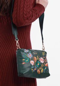 Zelená kožená kabelka se barevným květinovým vyšíváním a odepinatelným ramenním popruhem, s hladkou texturou a obdélníkovým tvarem.