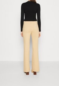 Beige, hochtaillierte Schlaghose mit glatter Textur und zwei Gesäßtaschen. Kombiniert mit einem figurbetonten, schwarzen Langarmoberteil.