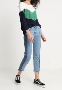 Trójkolorowa bluzka z długim rękawem w białym, zielonym i granatowym kolorze; luźny krój, zestawiona z jasnoniebieskimi dżinsami i czarnymi trampkami z białymi akcentami.