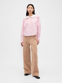 Stripet rosa skjorte med hvit krage, sammen med beige vide corduroy-bukser. Svarte sko fullfører antrekket.