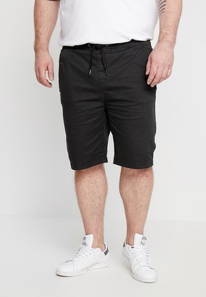 Shorts en coton noir avec une taille à cordon, arrivant juste au-dessus des genoux. Associés à des baskets blanches et une chemise blanche à manches courtes.