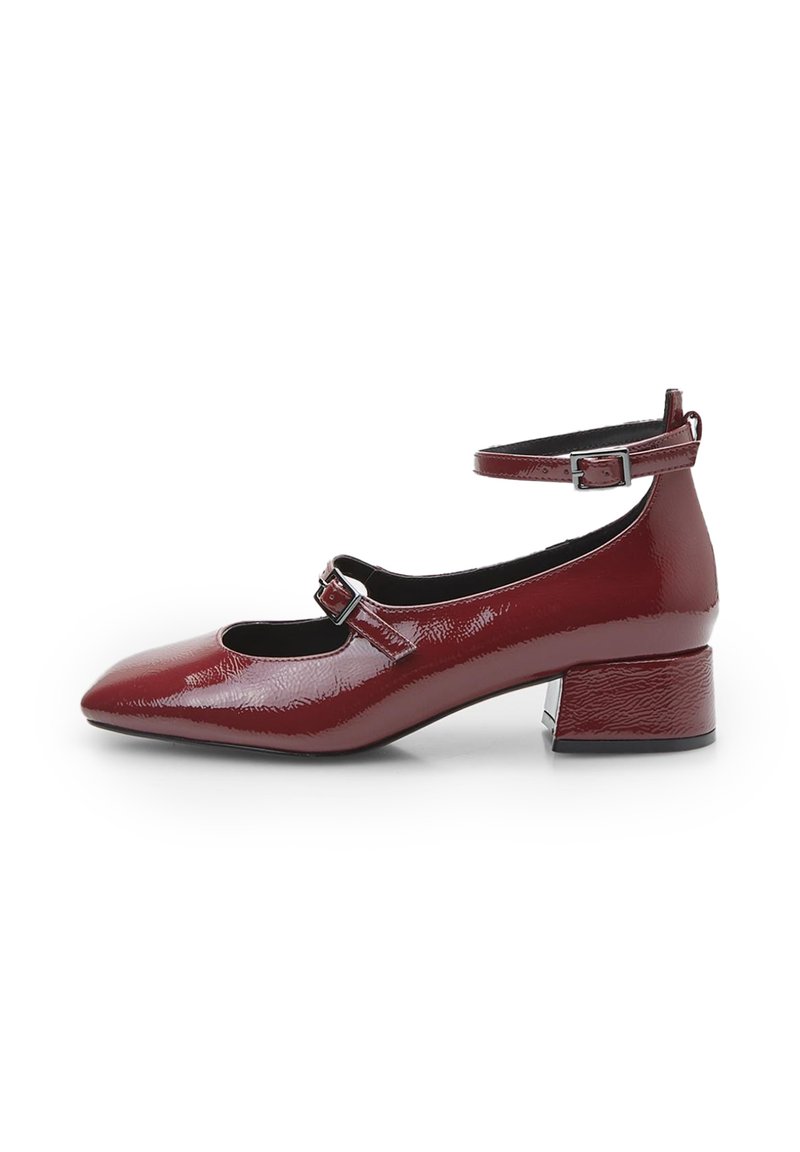 Red patent leather Mary Jane shoes with a pointed toe, ankle strap, and a textured block heel. Features two small cutouts on the front.