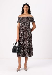Off-shoulder klänning i midilängd med en figursydd bodice i brunt och svart leopardmönster. Bärs med grå klackar och en svart handväska.