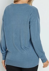 Ljusa blå stickad tröja med avslappnad passform, ribbade muddar och fåll, med mjuk textur och klassisk rund halsringning.