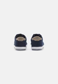 Baskets en toile navy avec une texture lisse, présentant un accent de talon en daim beige et des semelles en caoutchouc blanches, vues de l'arrière.
