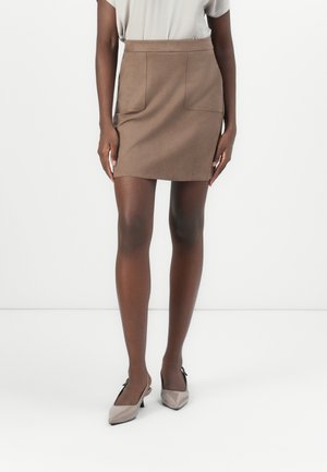 Brun suedet mini-skjørt med to frontlommer, en tettsittende midje og en glatt tekstur, parret med lys taupe spisse sko.