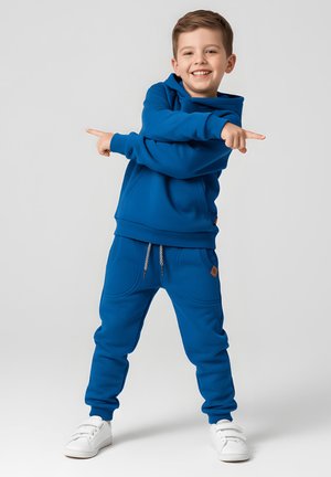 Niebieska bluza z kapturem i spodnie dresowe wykonane z miękkiego materiału, z prążkowanym obszyciem, dwoma bocznymi kieszeniami, sznurkiem oraz białe sneakersy.