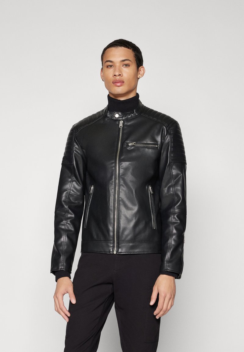 Black leather jacket with a zip closure, stand collar, ribbed shoulder accents, and two side zip pockets, worn over a black turtleneck.
