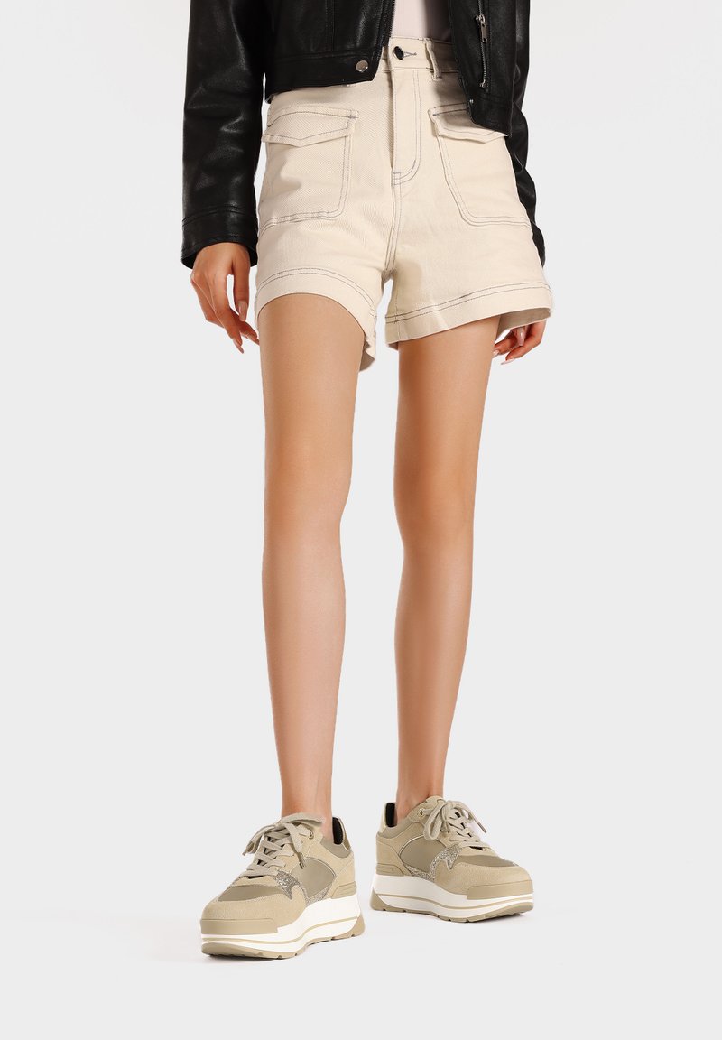 Shorts in denim beige con orli arrotolati e due tasche frontali, abbinati a sneakers beige e grigie con pannelli texturizzati e una suola bianca.