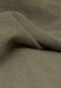 Nærbillede af olivengrønt strikket stof med synlig vævtekstur og bløde folder.