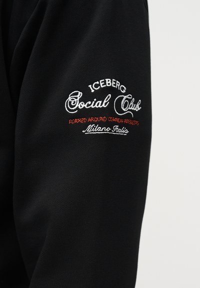 Μαύρο ύφασμα με κεντημένο κείμενο σε λευκό και κόκκινο που γράφει "ICEBERG Social Club Formed Around Common Interests Milano Italia."
