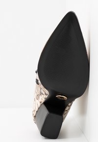 Zapato de tacón alto con puntera triangular, textura de piel de serpiente sintética en beige y marrón, y suela de goma negra con diseño estriado.