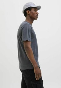 Grå kortærmet t-shirt i blødt bomuldsstof, rund halsudskæring, parret med sorte cargo-bukser med sidelommer, fanget i profil.