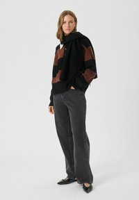 Zwart en bruin gestreepte trui met een hoge hals, gecombineerd met donkergrijze jeans. De look wordt compleet gemaakt met zwarte puntige flats.